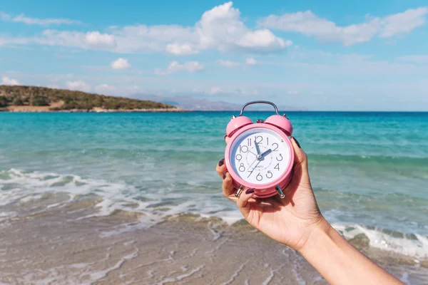 Kvinnas Hand Håller Rosa Väckarklocka Stranden Bakgrunden Sommar Semester Koncept — Stockfoto