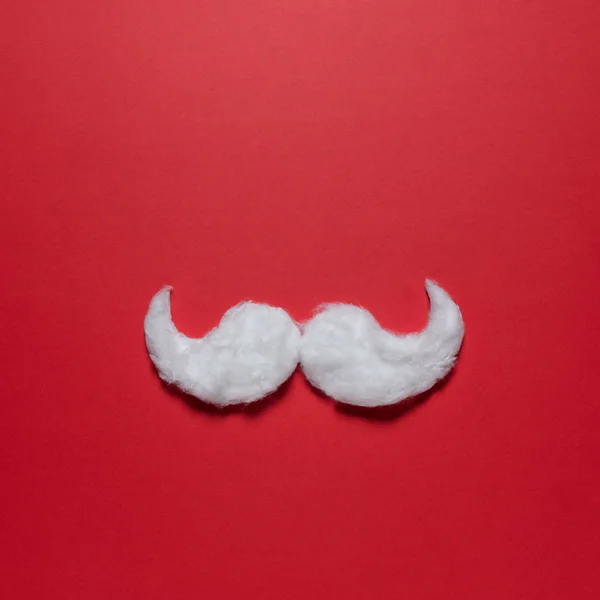 White hipster mustache of Santa Claus on red background. New Year or Christmas minimal concept.