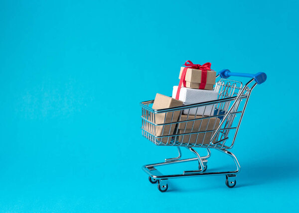 Gift boxes in shopping cart on blue background. Minimal sale concept.