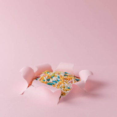Canlı pembe yırtık kağıt ile renkli arka plan sprinkles. En az soyut kavram.