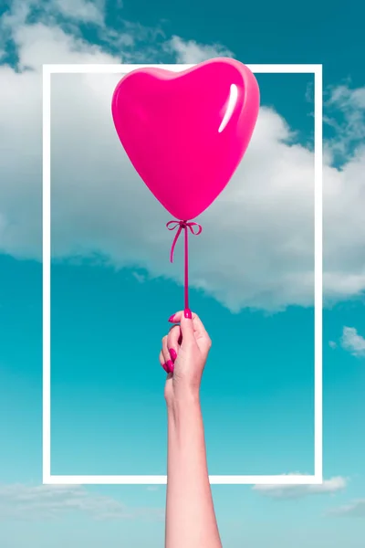 Womans hand with heart shaped balloon on background of sky. Love concept.