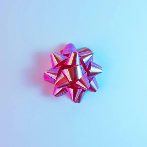 プラスチック装飾クリスマス ギフトは、活気に満ちた大胆なグラデーション ホログラム色で弓します。クリスマスと新年のミニマル ・ アート コンセプト. — ストック写真
