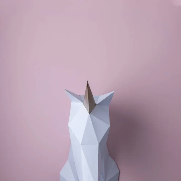 White 3d papercraft model of unicorn head on pink background. Minimal art concept.