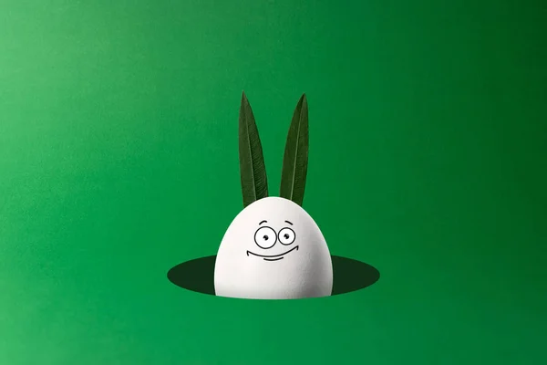 Œuf de Pâques avec des oreilles de lapin et drôle de visage regardant du trou. Concept minimal . — Photo