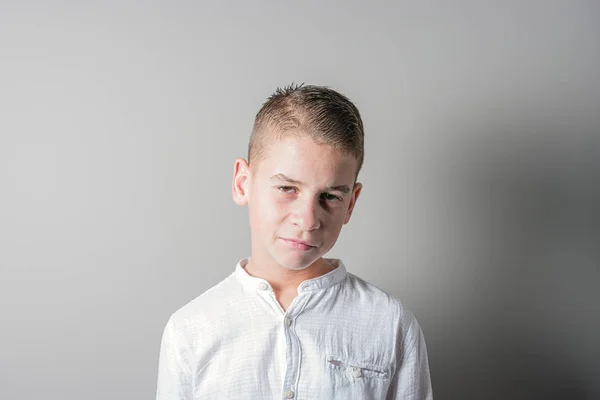 Triste garçon mignon dans une chemise blanche sur fond lumineux . — Photo