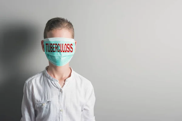 Niño con una máscara médica con inscripción roja TUBERCULOSIS en la cara sobre fondo brillante . — Foto de Stock