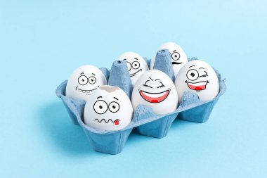 Paskalya yumurtaları ile mavi arka plan üzerine karton tepsisinde komik surat. En az kavramı.