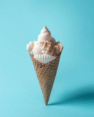 Deniz kabuklarını ve pastel mavi zemin üzerine dondurma koni ile yaratıcı kompozisyon. Yaz en az kavramı.