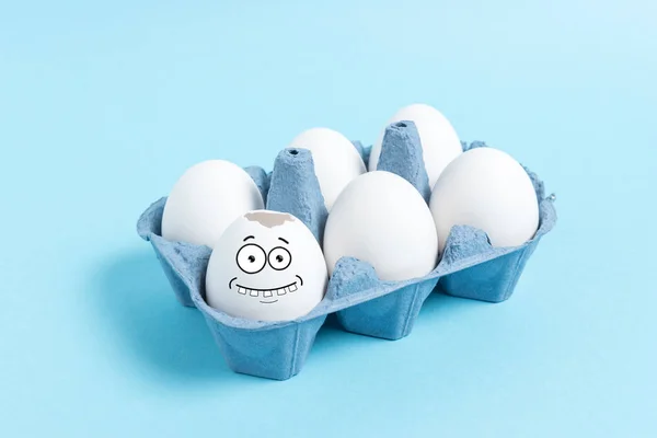 Easter eggs with funny face in carton tray on blue background. Minimal concept.