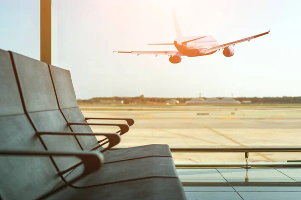 Lege stoelen in de vertrekhal op luchthaven op achtergrond van vliegtuig opstijgen bij zonsondergang. Travel concept. — Stockfoto