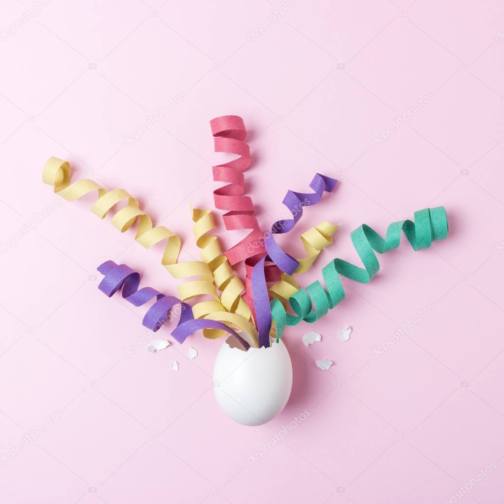 White Egg with party streamers on pink background. Minimal Easter concept. Flat lay.