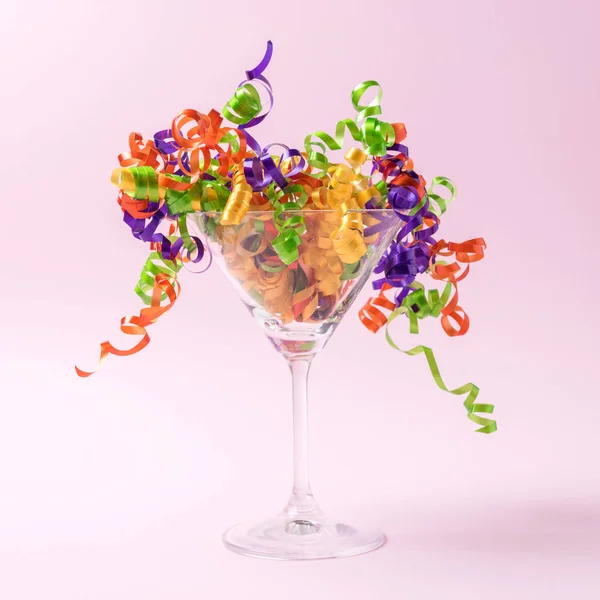 Martini glass with party streamers on a pink background. Minimal party concept.