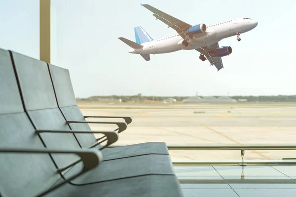 Puste krzesła w hali odlotów na lotnisku na tle samolotu startu. Koncepcja podróży. — Zdjęcie stockowe