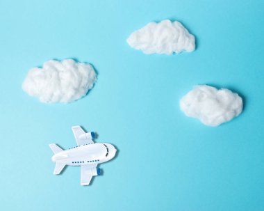 Beyaz pamuklu bulutlar ve pastel mavi arka planda küçük bir uçak. Asgari konsept.