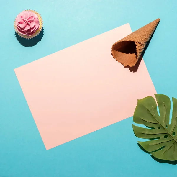 Hoja de palma tropical con cupcake y cono de helado sobre fondo azul brillante. Composición mínima de verano. Puesta plana . — Foto de Stock