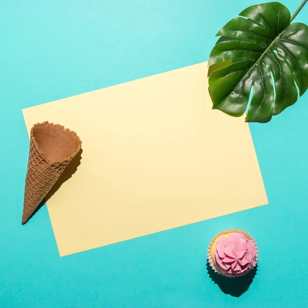 Hoja de palma tropical con cupcake y cono de helado sobre fondo azul brillante. Composición mínima de verano. Puesta plana . — Foto de Stock