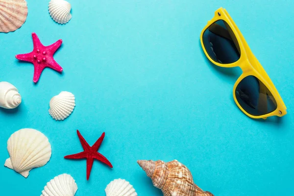 Composizione creativa con conchiglie e occhiali da sole gialli su sfondo blu. Concetto estate minima . — Foto Stock