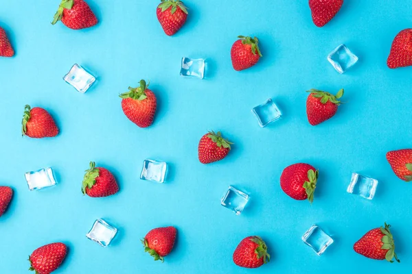 五颜六色的图案,由草莓制成,蓝色背景上有冰块。最小的夏季概念. — 图库照片