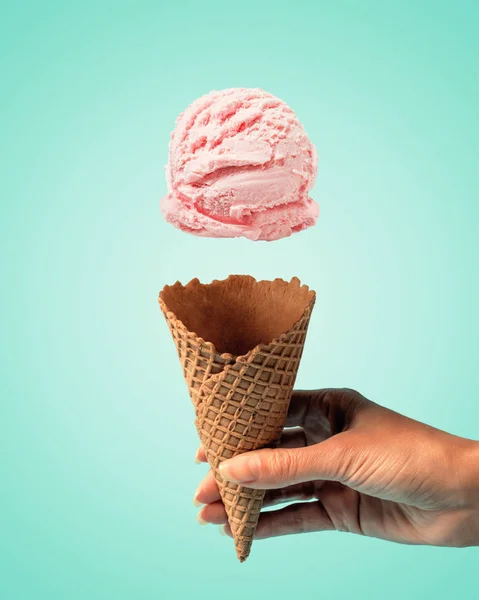 Cuchara de helado rosa con cono de helado en la mano sobre fondo brillante. Concepto de verano mínimo . — Foto de Stock
