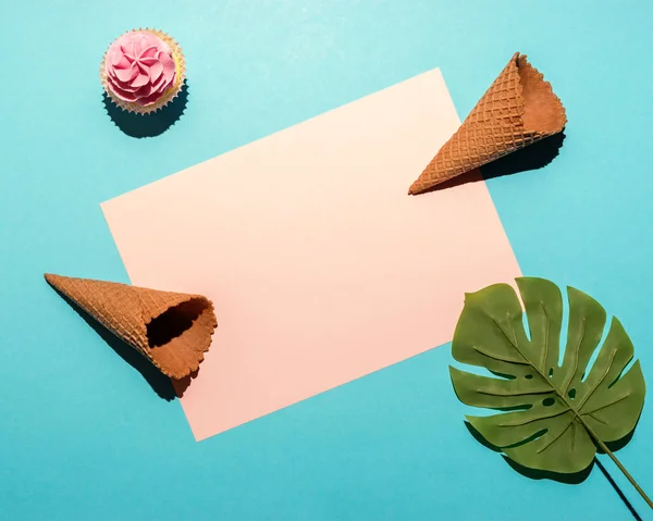 Hoja de palma tropical con cupcake y cono de helado sobre fondo azul brillante. Composición mínima de verano. Puesta plana . — Foto de Stock