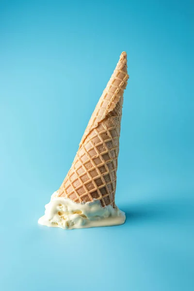Melted ice cream with ice cream cone on pastel blue background.