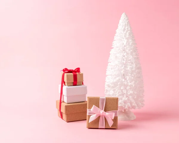 Besneeuwde kerstboom met geschenkdozen op pastel roze achtergrond. — Stockfoto