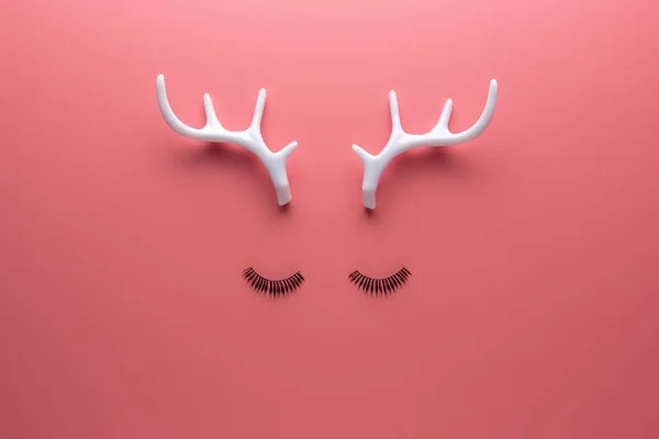 Christmas reindeer face made of eyelashes and white antlers on pink background. Minimal New Year or Christmas concept. Flat lay. — Stock Photo, Image