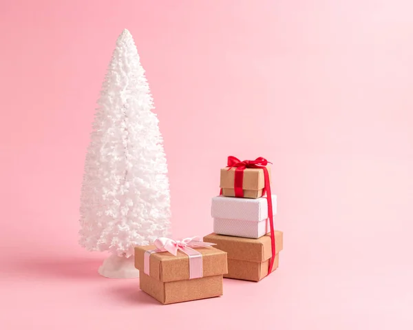 Besneeuwde kerstboom met geschenkdozen op pastel roze achtergrond. — Stockfoto