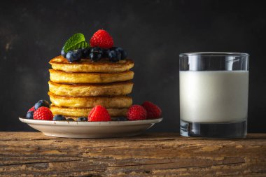 Taze böğürtlenli leziz krepler ve kırsal ahşap masada bir bardak süt. Yiyecek konsepti.