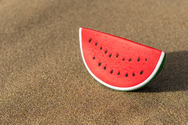 Watermelon toy on a sand background. Minimal summer vacation concept.
