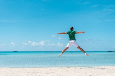 Kumsalda kollarını açmış zıplayan mutlu genç adam. Yaz tatili kavramı.