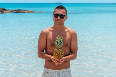 Kumsalda ananaslı mutlu bir genç adam. Yaz tatili kavramı.