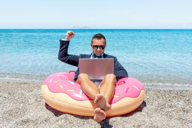 Tropikal sahilde şişme donutta dizüstü bilgisayarı olan mutlu bir iş adamı. Yaz tatili kavramı.