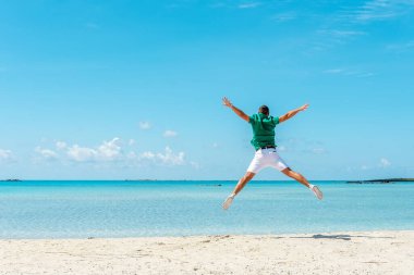 Kumsalda kollarını açmış zıplayan mutlu genç adam. Yaz tatili kavramı.