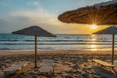 Günbatımında şemsiyeli tropik plaj manzarası. Tatil ve seyahat kavramı.