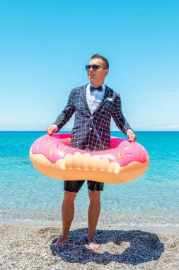 Tropikal bir plajda şişme donutla ceketli mutlu bir iş adamı. Yaz tatili kavramı.
