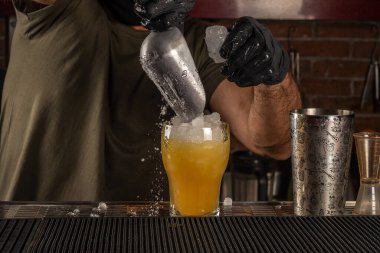 Bardaki barmen turuncu alkollü bir kokteylin içine buz koyuyor. Yaz partisi geçmişi.