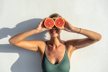 Güzel, genç bir kadın, ellerinde, gözlerinin yanında tatlı bir greyfurt tutuyor. Moda yaz konsepti.