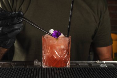 Bardaki barmen buzlu ve çiçekli alkollü kokteyl yapıyor. Yaz partisi geçmişi.