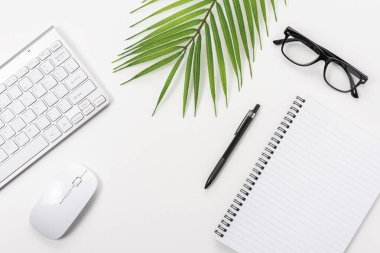 Boş defter, bilgisayar klavyesi ve diğer ofis malzemeleriyle dolu beyaz ofis masası. Kopyalama alanı olan üst görünüm.