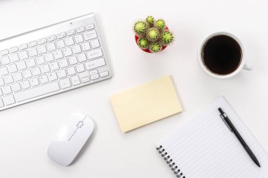 Boş defter, bilgisayar klavyesi ve diğer ofis malzemeleriyle dolu beyaz ofis masası. Kopyalama alanı olan üst görünüm.