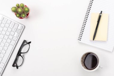 Bilgisayar klavyesi, ofis malzemeleri ve beyaz arka planda kahve fincanı olan çalışma alanı. Kopyalama alanı olan üst görünüm.