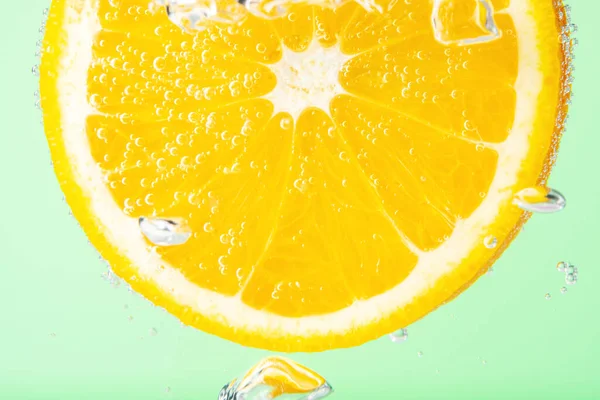 Close up view of a slice of orange in soda water with bubbles. Summer drink concept.