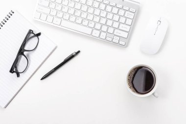 Bilgisayar klavyesi, ofis malzemeleri ve beyaz arka planda kahve fincanı olan çalışma alanı. Kopyalama alanı olan üst görünüm.
