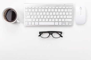 Bilgisayar klavyesi, ofis malzemeleri ve beyaz arka planda kahve fincanı olan çalışma alanı. Kopyalama alanı olan üst görünüm.