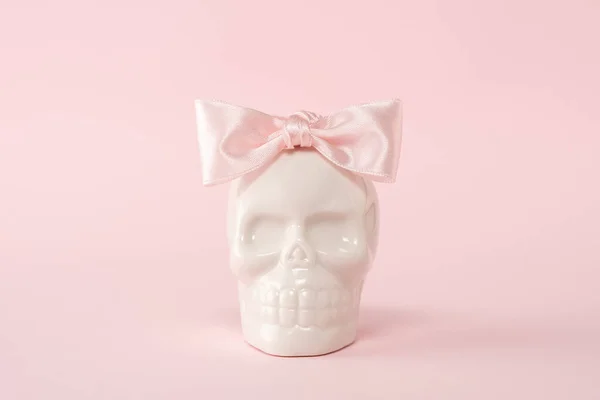 White skull with pink bow tie on a pink background. Minimal Halloween spooky girl concept.