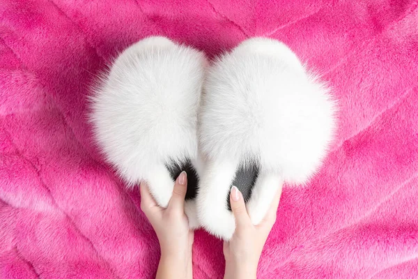 Female hands holding beautiful fur slippers on the fluffy fur plaid. Flat lay.