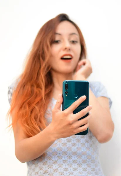 Cep telefonu açık ağzıyla konuşan, cep telefonu profil görüntüsüne bakan kızıl saçlı bir kız. beyaz arkaplan