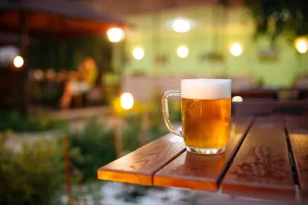 Beer with foam outside blurry lights background