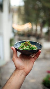 Elinde yeşil chuka deniz yosunu salatasıyla siyah kase var.